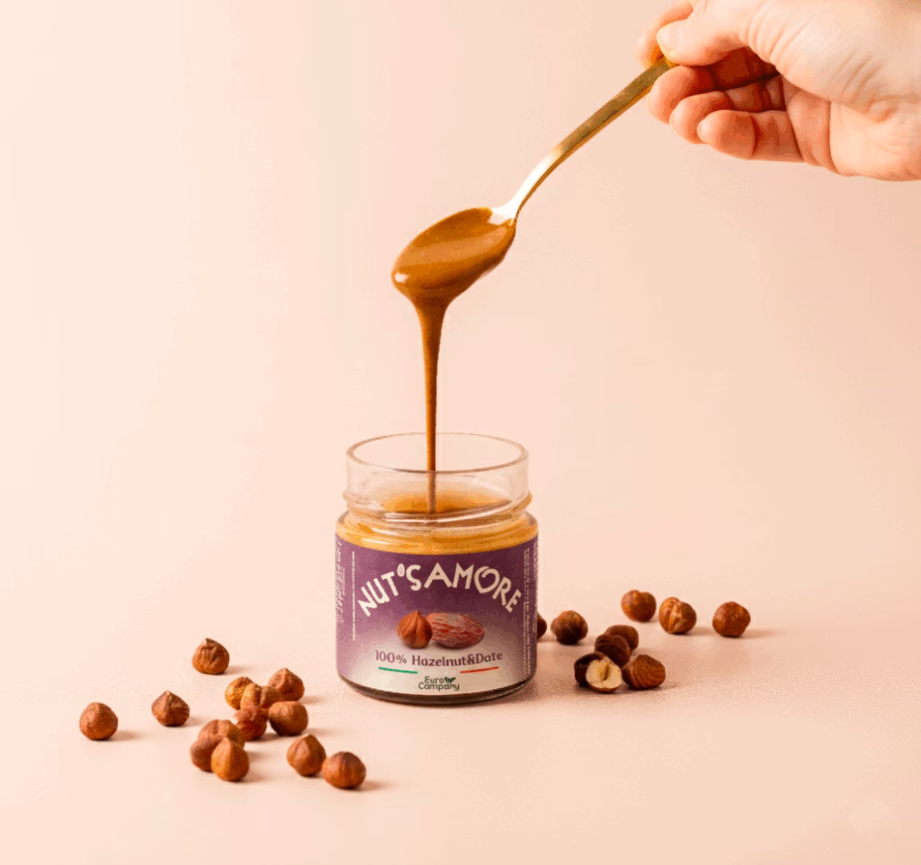 Hand holding spoon pouring Nut's Amore 100% Hazelnut & Date spread into a jar